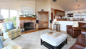 A spacious living room with a fireplace, a dining area with wooden cabinets, and a large window providing a view of the outdoors.