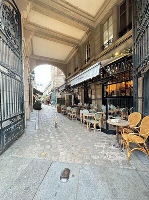 A cobblestone street with outdoor seating, a wrought iron gate, and a covered passageway. - OPULENCE IN ODÉON: DELUXE APARTMENT STEPS FROM HISTORIC LUXEMBOURG GARDENS (Paris)