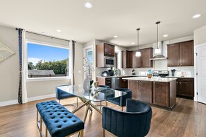 A modern kitchen with a glass dining table, dark wooden cabinets, and a large window offering a view of the outdoors. - PY1: Charming 4-bedroom house in Puyallup with WiFi, AC (Puyallup)