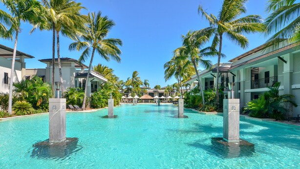 Een helderblauw zwembad met palmbomen en moderne gebouwen op de achtergrond.