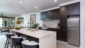 Een moderne keuken met donkerhouten kastjes, een roestvrijstalen koelkast, een groot kookeiland met barkrukken en een betegelde spatwand.