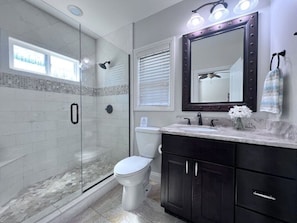 A bathroom with a glass-enclosed shower, a toilet, a vanity with a mirror, and a towel rack. - Destination #06 (Anaheim)