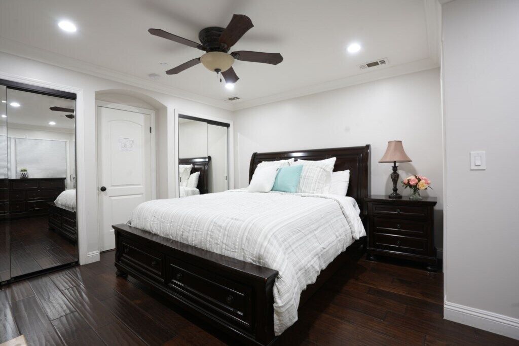 A bedroom with a bed, a ceiling fan, a dresser, a nightstand, and a mirror.