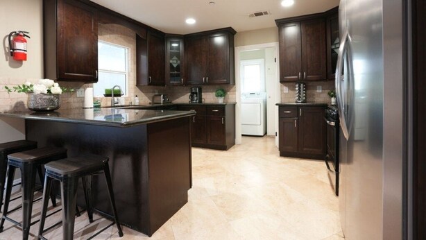 A kitchen with dark wooden cabinets, a central island with stools, a refrigerator, and a coffee maker. - Sweet 5 Bedroom, 4 Bath Pool Home 1/2 Mile Walk To Disney (Anaheim)