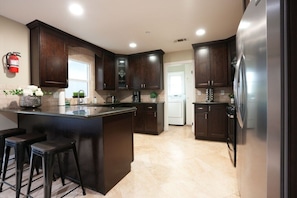 A kitchen with dark wooden cabinets, a central island with stools, a refrigerator, and a coffee maker. - Sweet 5 Bedroom, 4 Bath Pool Home 1/2 Mile Walk To Disney (Anaheim)