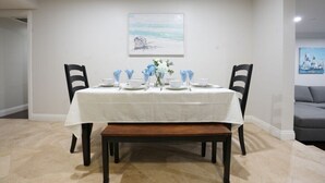 A dining room with a white table set for four, two chairs on each side, a bench, and a painting on the wall. - Sweet 5 Bedroom, 4 Bath Pool Home 1/2 Mile Walk To Disney (Anaheim)