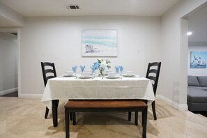 A dining room with a white table set for four, two chairs on each side, a bench, and a painting on the wall. - Sweet 5 Bedroom, 4 Bath Pool Home 1/2 Mile Walk To Disney (Anaheim)
