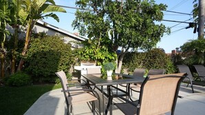 An outdoor patio with a table and chairs, surrounded by greenery and a building in the background. - Sweet 5 Bedroom, 4 Bath Pool Home 1/2 Mile Walk To Disney (Anaheim)