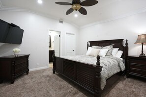 Ein Schlafzimmer mit einem Bett, einem Deckenventilator, einem Fernseher, einer Kommode und einer Lampe.
