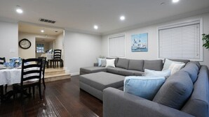A living room with a gray sofa, a dining table with chairs, and a clock on the wall. - Sweet 5 Bedroom, 4 Bath Pool Home 1/2 Mile Walk To Disney (Anaheim)