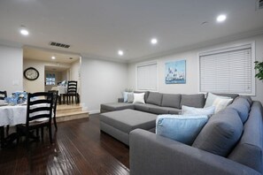 A living room with a gray sofa, a dining table with chairs, and a clock on the wall. - Sweet 5 Bedroom, 4 Bath Pool Home 1/2 Mile Walk To Disney (Anaheim)