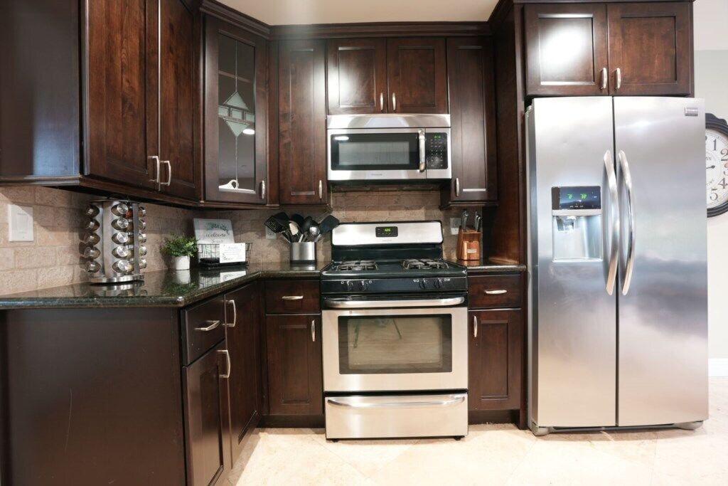 Une cuisine avec des meubles en bois foncé et des appareils électroménagers en acier inoxydable, notamment un four à micro-ondes, une cuisinière, un four et un réfrigérateur.