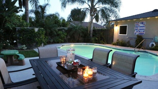 A poolside area with a table set for dining, surrounded by chairs, and a sign with diving and swimming information. - Sweet 5 Bedroom, 4 Bath Pool Home 1/2 Mile Walk To Disney (Anaheim)