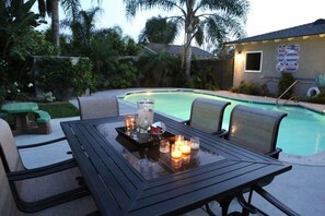 A poolside area with a table set for dining, surrounded by chairs, and a sign with diving and swimming information. - Sweet 5 Bedroom, 4 Bath Pool Home 1/2 Mile Walk To Disney (Anaheim)