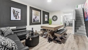 A modern living room with a black leather sofa, a wooden dining table, and artwork on the walls. - Cozy & Stylish/Pool Table & Fun

 (Camden)