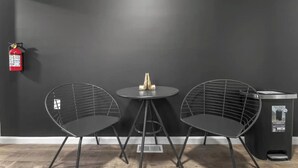 A room with two black wireframe chairs, a small round table with a gold object, and a black trash bin. A fire extinguisher is mounted on the wall. - Cozy & Stylish/Pool Table & Fun

 (Camden)