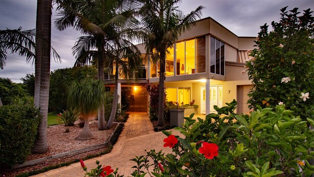 A modern two-story house with a paved pathway leading to the entrance, surrounded by lush greenery and palm trees. - Absolute lake frontage property located in the heart of beautiful Mallacoota.  (Mallacoota)