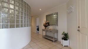 A clean, modern hallway with a curved glass wall, a wooden console table with decorative items, a mirror, and a door. - Absolute lake frontage property located in the heart of beautiful Mallacoota.  (Mallacoota)