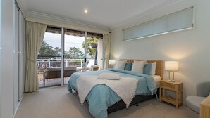 A bedroom with a large bed, a nightstand with a lamp, a chair, and a view through a sliding glass door to an outdoor area. - Absolute lake frontage property located in the heart of beautiful Mallacoota.  (Mallacoota)