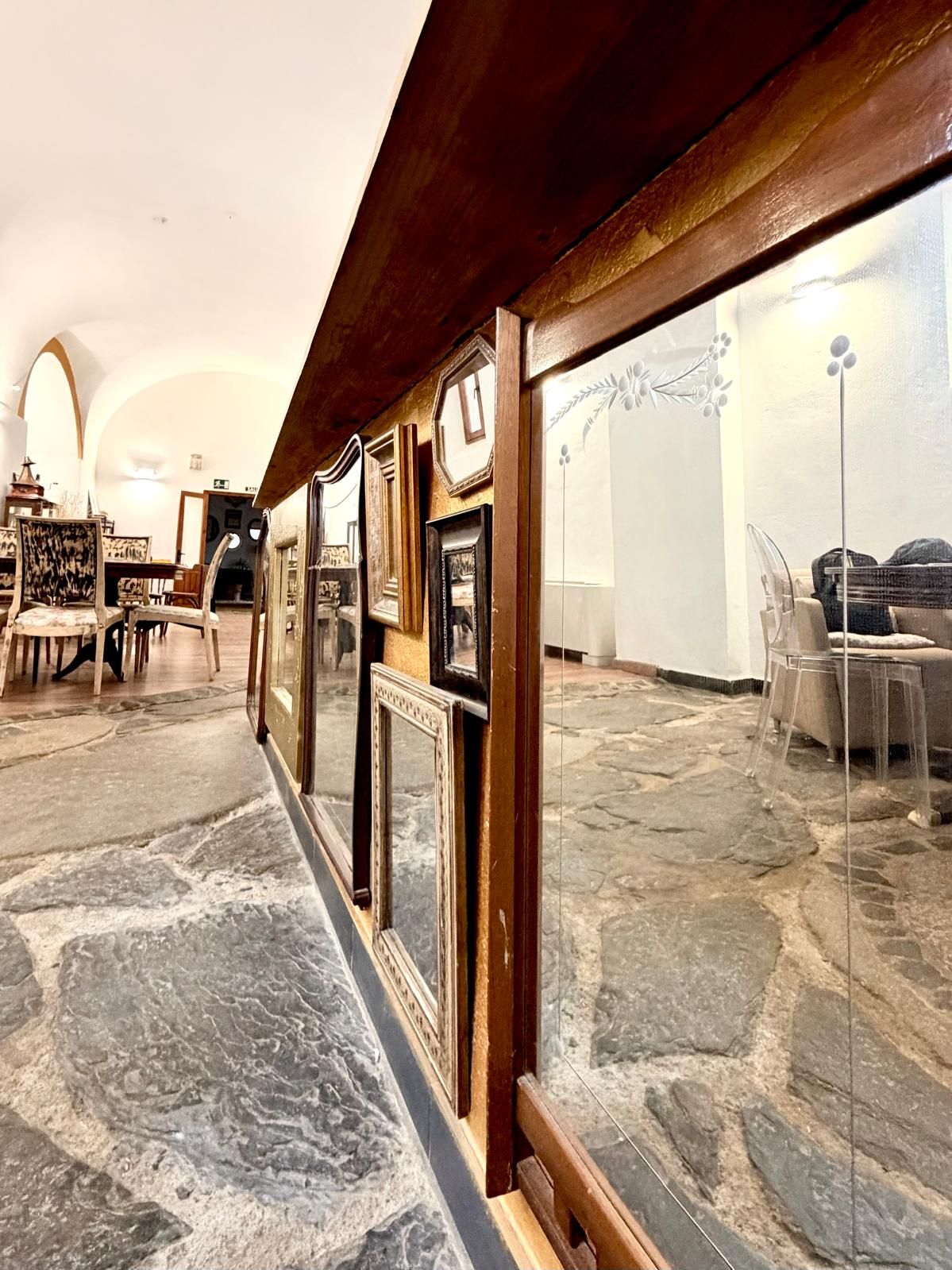 Un pasillo con suelo de piedra, marcos de madera y una zona de estar con mesa y sillas.