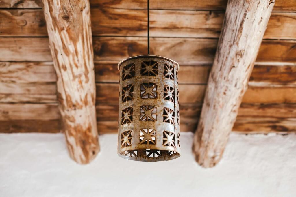 A hanging metal lantern with star-shaped cutouts, suspended from a wooden ceiling with exposed beams.