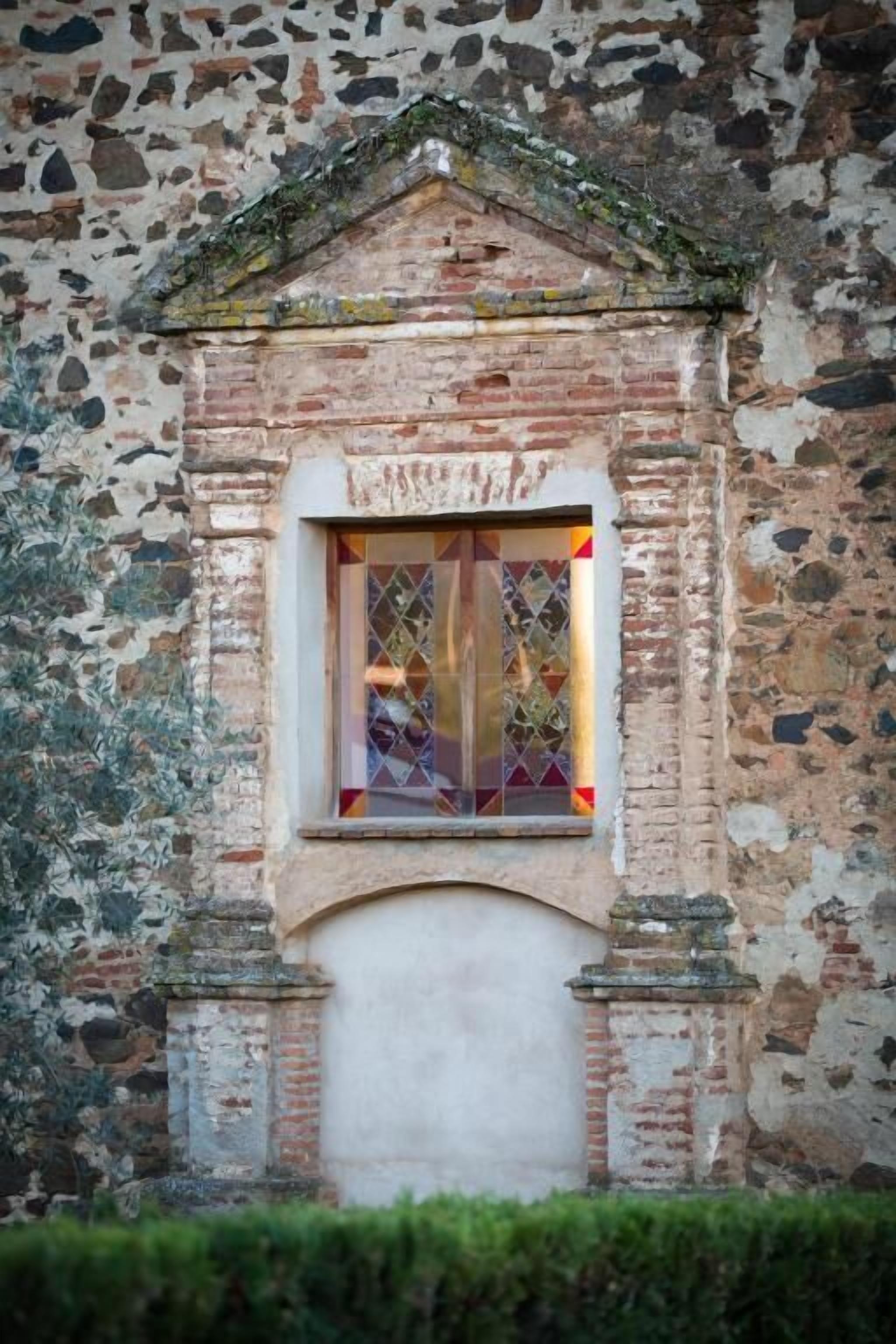 A stone building with a window featuring stained glass.