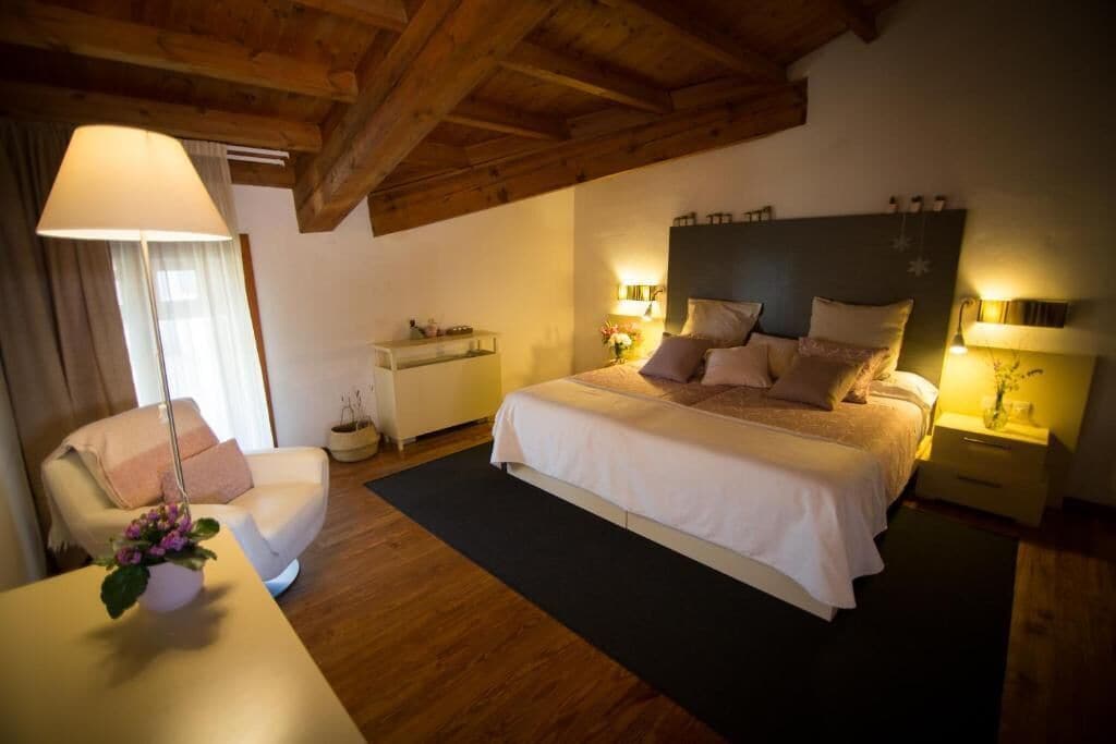 A bedroom with a large bed, bedside tables with lamps, a chair, a small table with a plant, and a wooden ceiling.