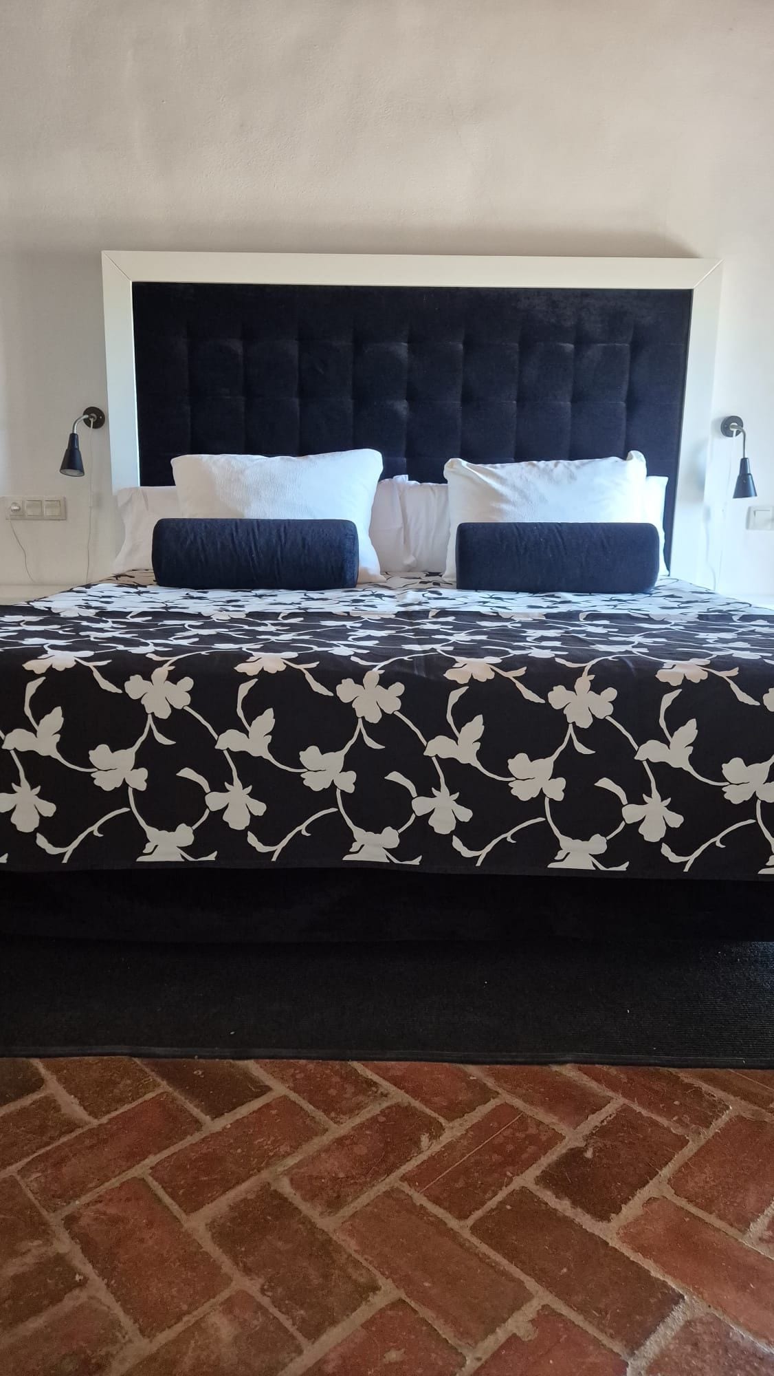A bed with a black and white floral bedspread, a dark headboard, and two bedside lamps.