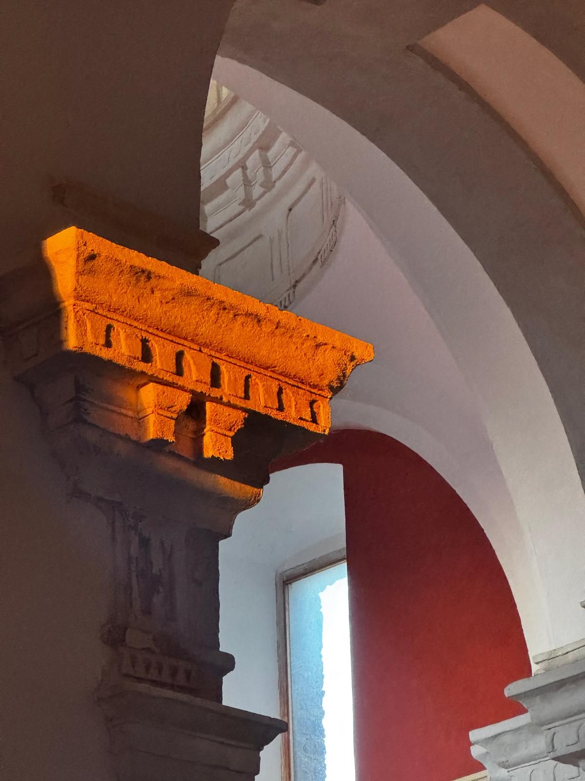 A room with a red wall, a white arched doorway, and a column with a textured surface.