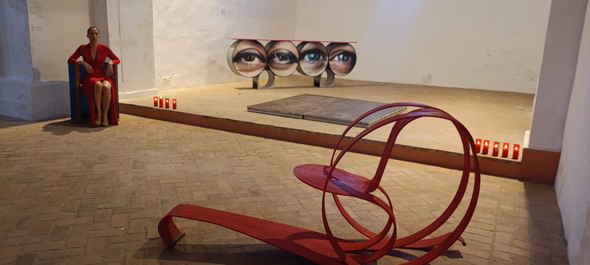 An art installation with a sculpture and a series of eye-like images on the wall.