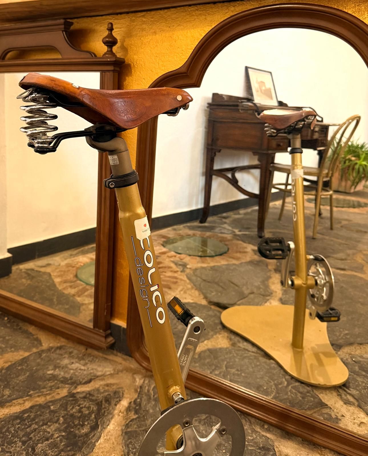 Una bicicleta antigua con asiento de cuero y estructura dorada, sobre un piso con diseño.