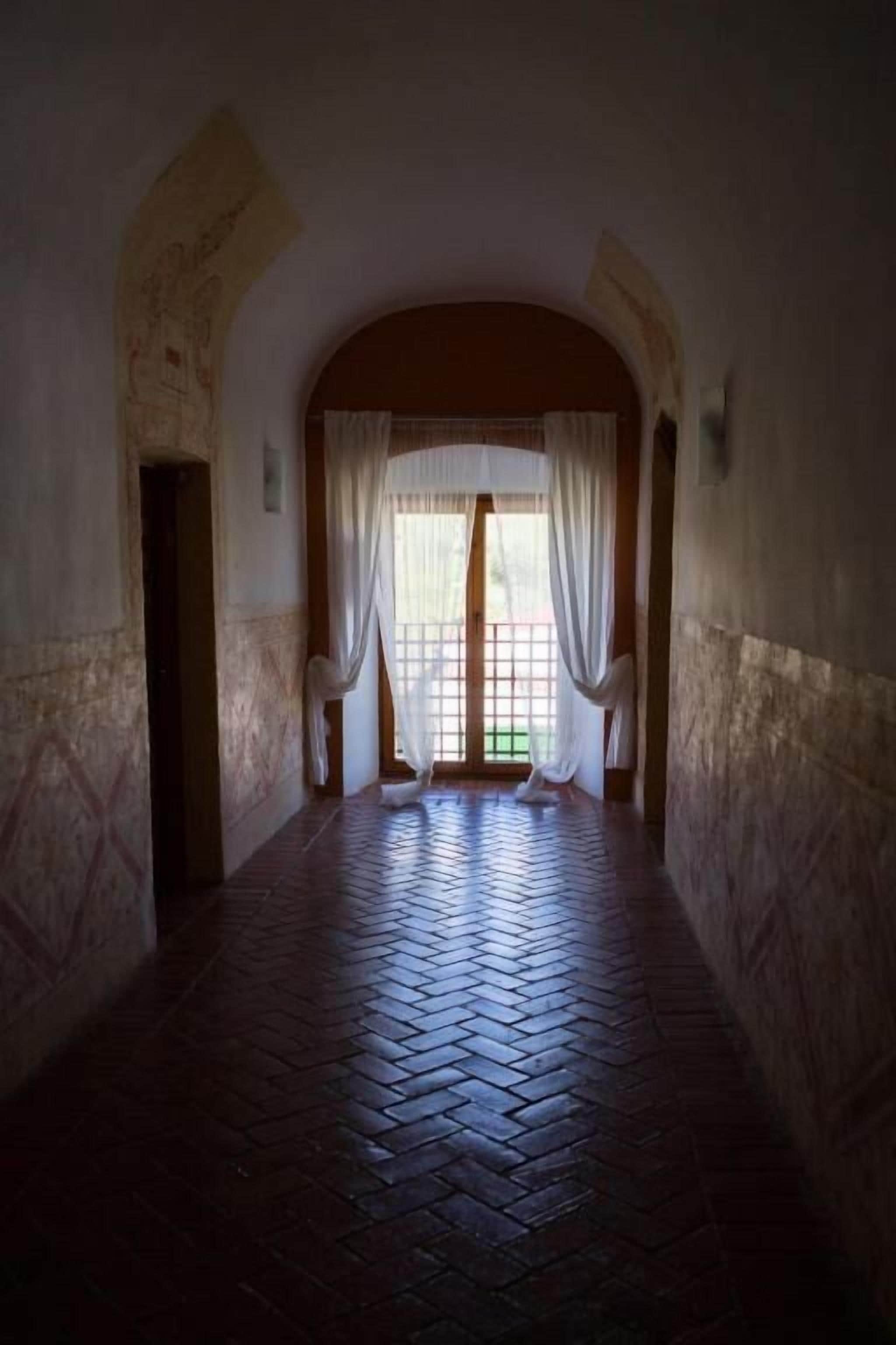 A corridor with a tiled floor, an arched doorway, and a window with white curtains.