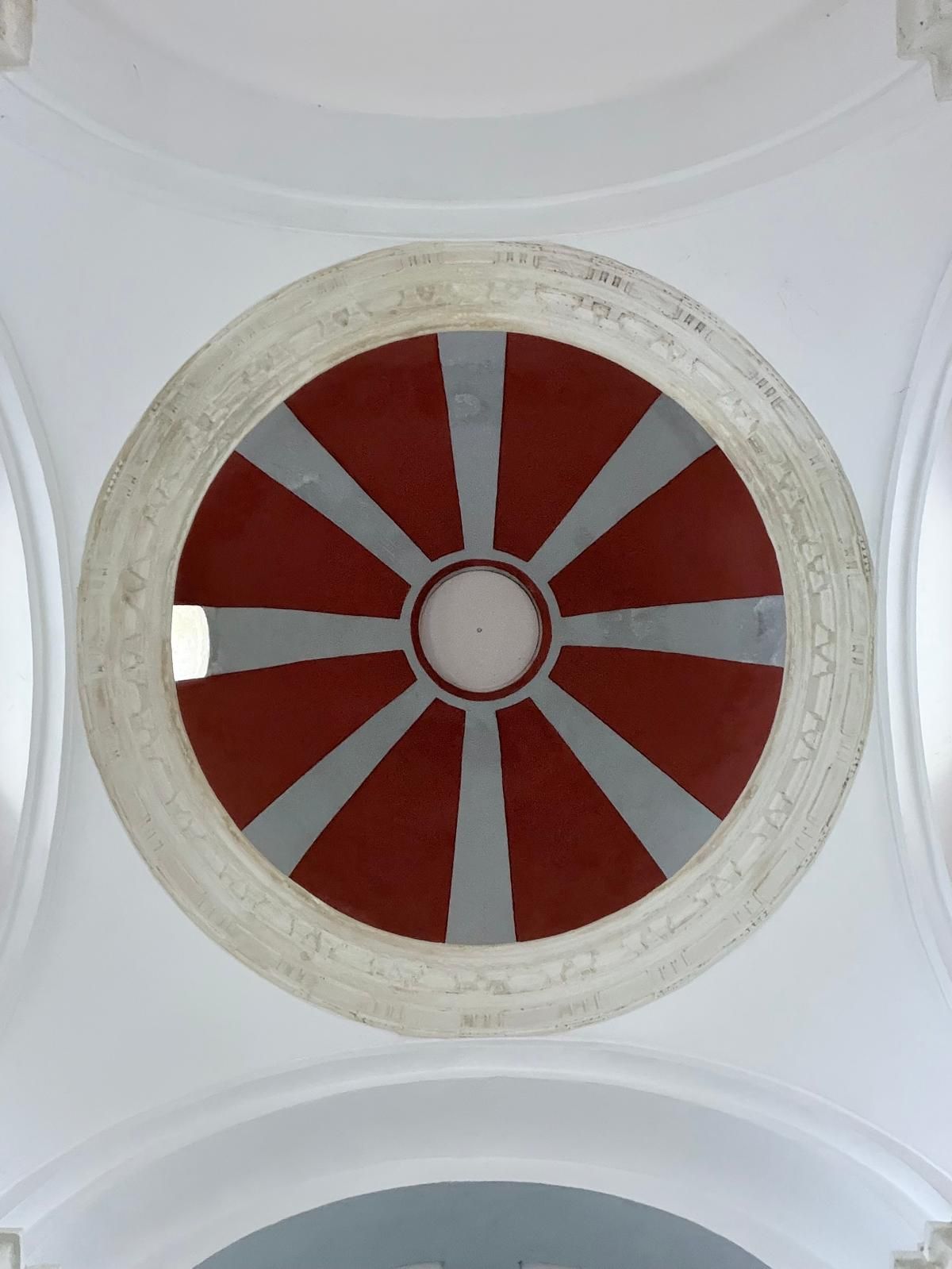 Elemento arquitectónico circular con un círculo blanco central rodeado de segmentos rojos y grises.