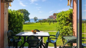 Eine Terrasse im Freien mit Tisch und Stühlen, Blick auf eine grüne Rasenfläche und ein Gebäude im Hintergrund.