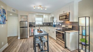 A modern kitchen with white cabinets, stainless steel appliances, and a central island with stools. - Beautiful one bedroom condo in Marco Island with so much to offer!  (Marco Island)