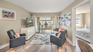 A modern living room with a flat-screen TV, a sofa, a coffee table, and a large window with a view of a balcony. - Beautiful one bedroom condo in Marco Island with so much to offer!  (Marco Island)