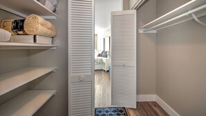 A walk-in closet with open louvered doors, shelves with folded towels, and a visible bedroom in the background. - Beautiful one bedroom condo in Marco Island with so much to offer!  (Marco Island)