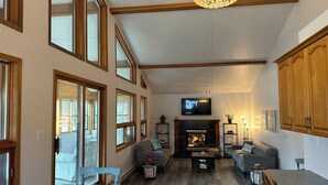 A spacious living room with a fireplace, large windows, and wooden beams.