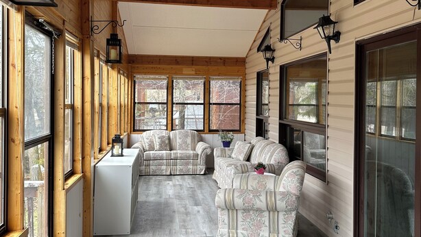 A covered porch with wooden beams, large windows, and two sofas.