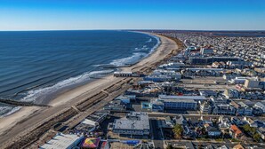 Vista aérea de un pueblo costero con playa, edificios residenciales y un puerto deportivo.