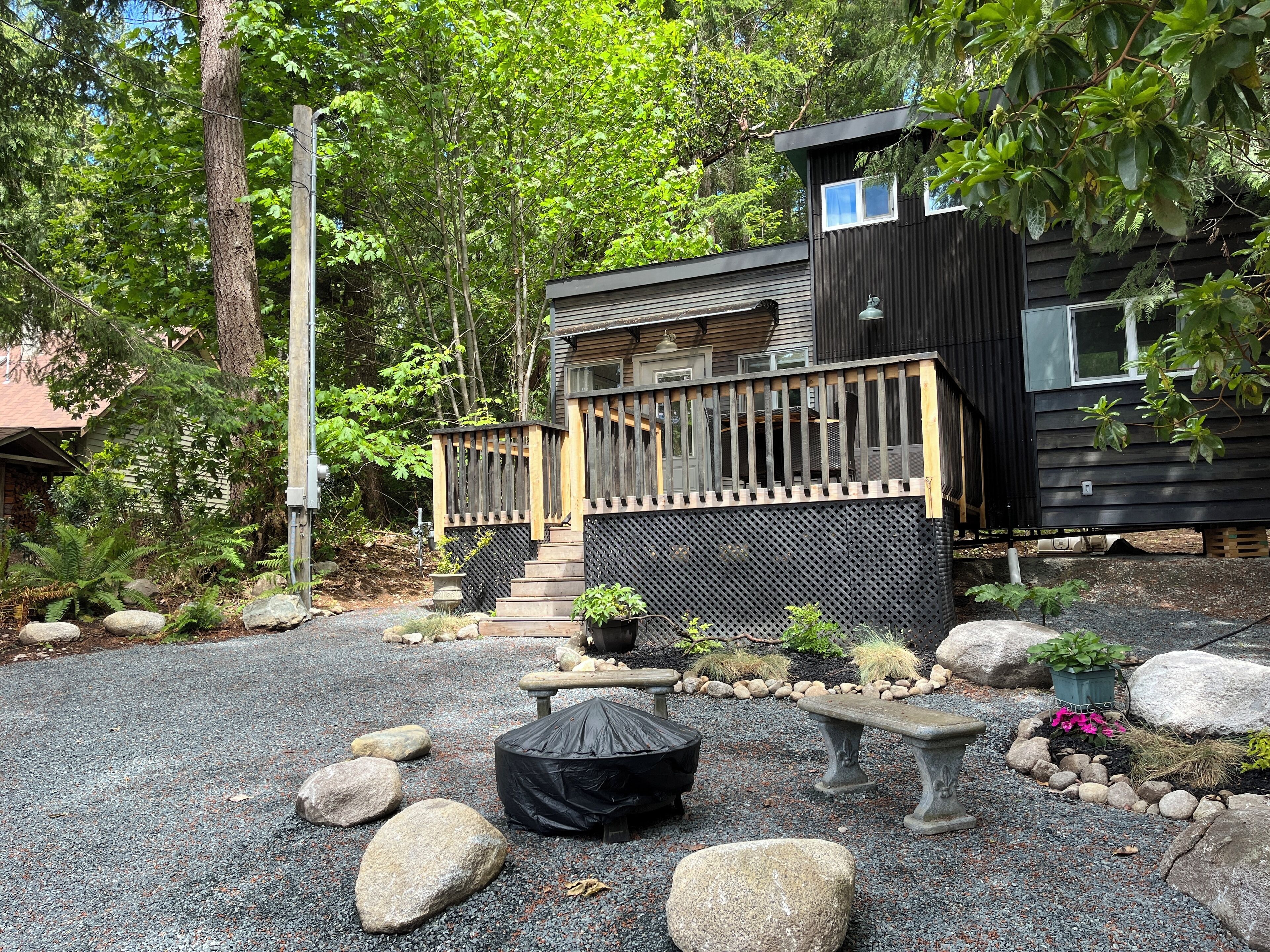 Une cabane moderne dotée d’une terrasse en bois, entourée d’un chemin de gravier et de gros rochers.