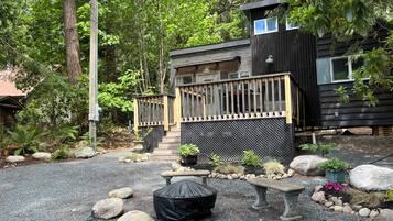 Une cabane moderne dotée d’une terrasse en bois, entourée d’un chemin de gravier et de gros rochers.