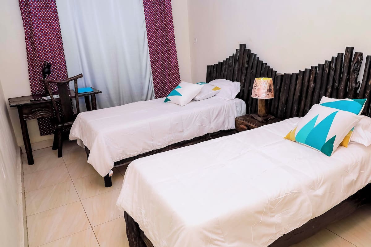 A hotel room with two single beds, a wooden nightstand, a small table, and a chair.