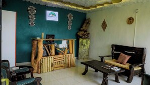 A cozy room with a wooden reception desk, a sofa with cushions, and a coffee table. - Banana Eco Resort (Kiziguro)