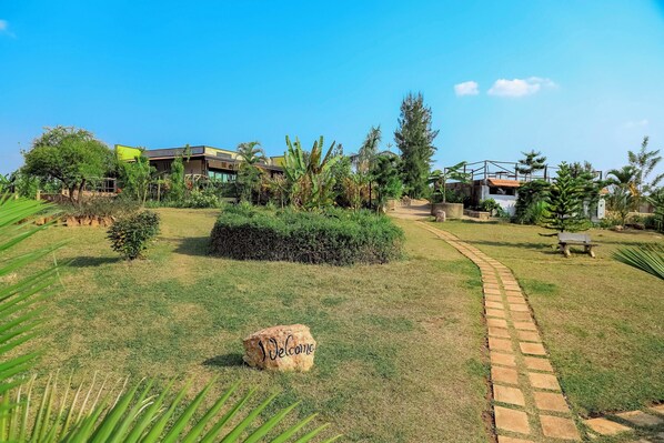 A well-maintained garden with a pathway leading to a building, surrounded by various plants and a 'Welcome' sign.