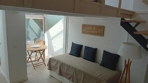 Ein Schlafzimmer mit einem Bett, einem Schreibtisch und einem Sessel. Es gibt ein Fenster mit Blick auf einen Balkon.