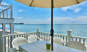 A seaside patio with white wicker chairs, a table, and a beige umbrella. - Charming 3 Bedroom Beach Front Cottage (Milford)