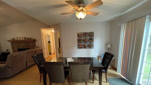 Un comedor con mesa y sillas, ventilador de techo, chimenea y ventana con cortinas.