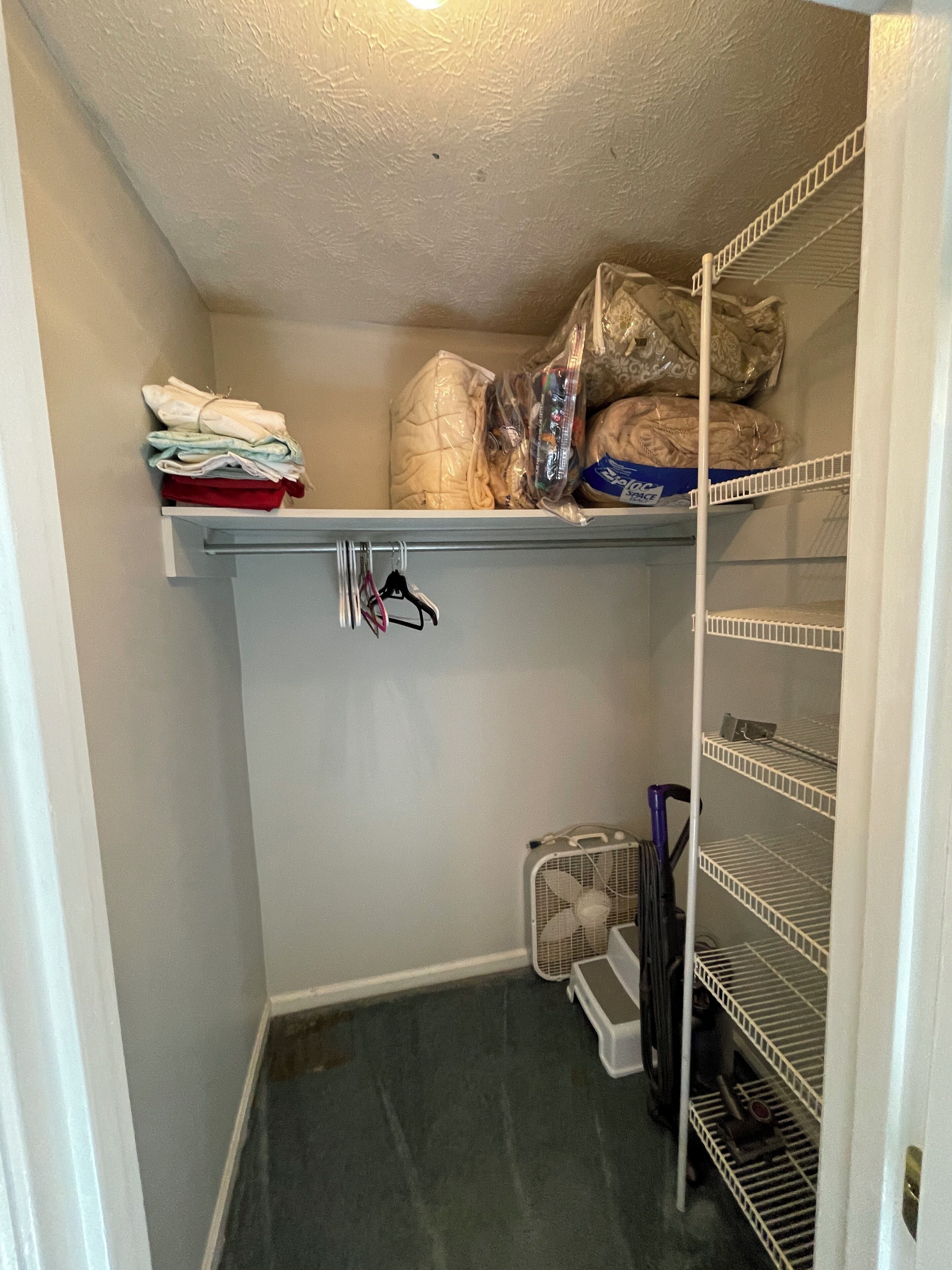 A storage closet with shelves, a fan, and a trash bin.
