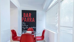 A modern interior with a glass table and red chairs, a blackboard menu, and a window with blinds.